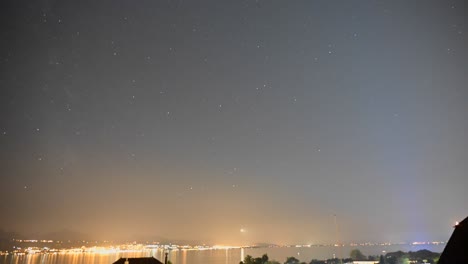 Noche-Estrellada-Sobre-El-Lago-De-Ginebra,-El-Cielo-Se-Mueve-Y-Las-Luces-De-Las-Ciudades-De-Evian-Y-Lausana-Crean-Un-Halo-De-Luz,-Lapso-De-Tiempo