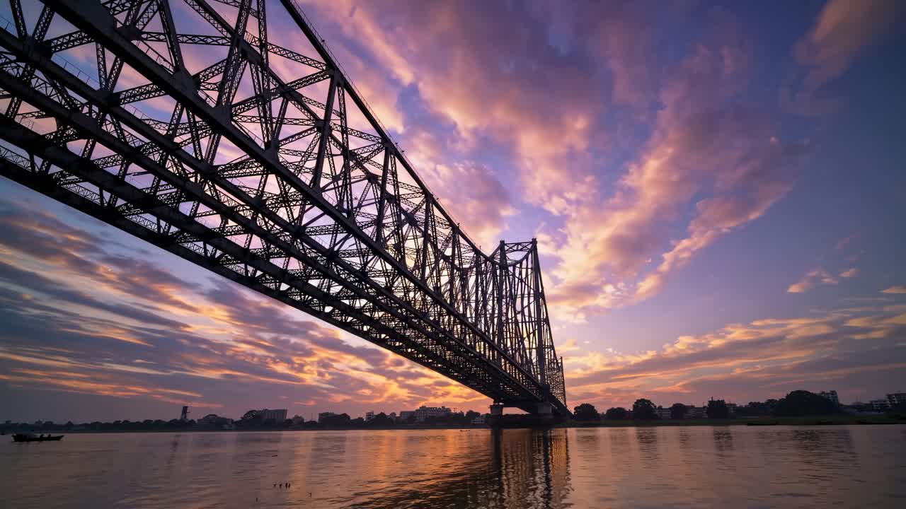 Vídeo dramático a contrapicado de un puente de acero al atardecer, que captura cielos y reflejos vibrantes