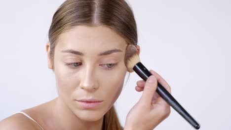 woman using makeup brush and applying powder