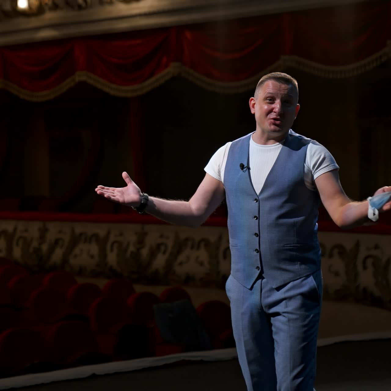 Presenter on stage. Man holding medical mask in his hand and talking on camera in empty theater. Portrait of middle-aged man speaker. Pandemic concept