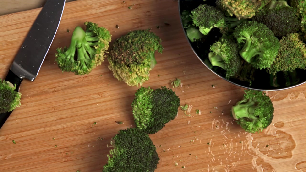 Cimette di broccoli freschi che cadono su un tagliere di legno