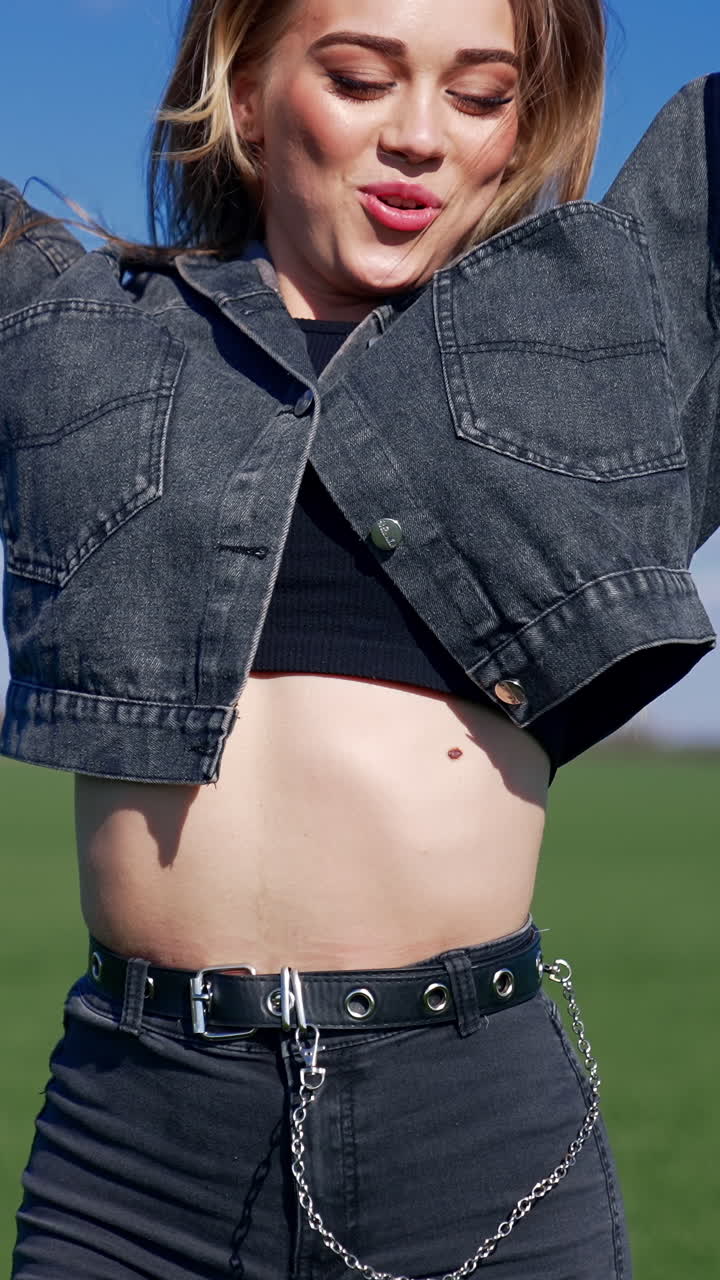 Portrait of a cheerful girl. Beautiful young woman in jeans jacket jumping and looking on camera on blur nature landscape in spring. Vertical video