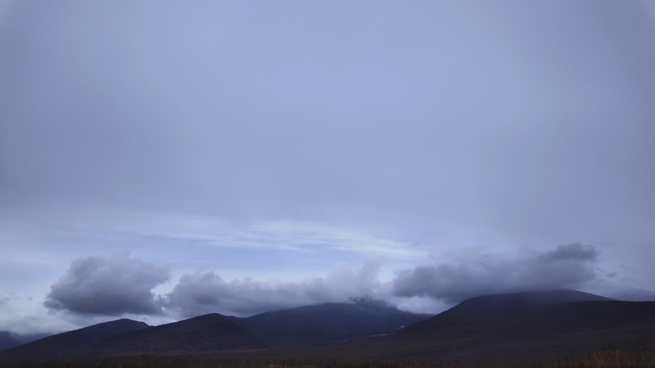 Witness the transformation of twilight as clouds dynamically shift over the mountainous terrain, showcasing the beauty of nature's changing light and atmosphere.