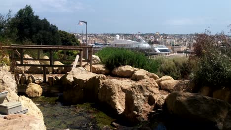 peaceful river fountain in herbert ganado park in floriana, malta with large cruise ship and the three cities in background