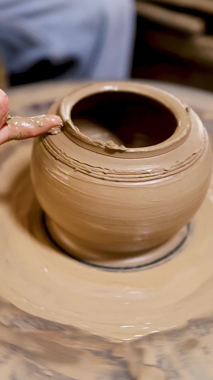 Primo piano del dito di un vasaio che rifinisce un vaso di argilla bagnata che gira in un laboratorio