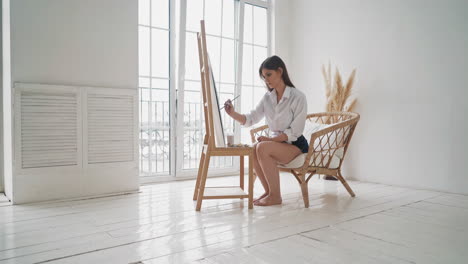 attractive woman draws painting on wooden easel in studio