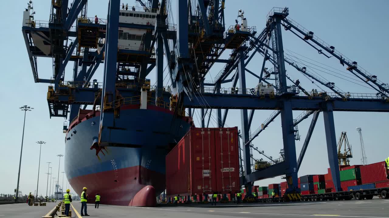 Dynamic low-angle video shot of a shipping port, capturing a container being loaded onto a cargo