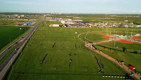 Statische-Drohnenaufnahme-Von-Leuten,-Die-Auf-Einem-Feld-Neben-Einer-Autobahn-Mit-Der-Stadt-Winnipeg-Im-Hintergrund-Fußball-Spielen