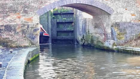 Schleusentore-öffnen-Sich-Und-Ein-Narrowboat-Taucht-Aus-Der-Schleuse-Auf-Einem-Kanal-Auf-Und-Fährt-Unter-Einer-Brücke-Hindurch