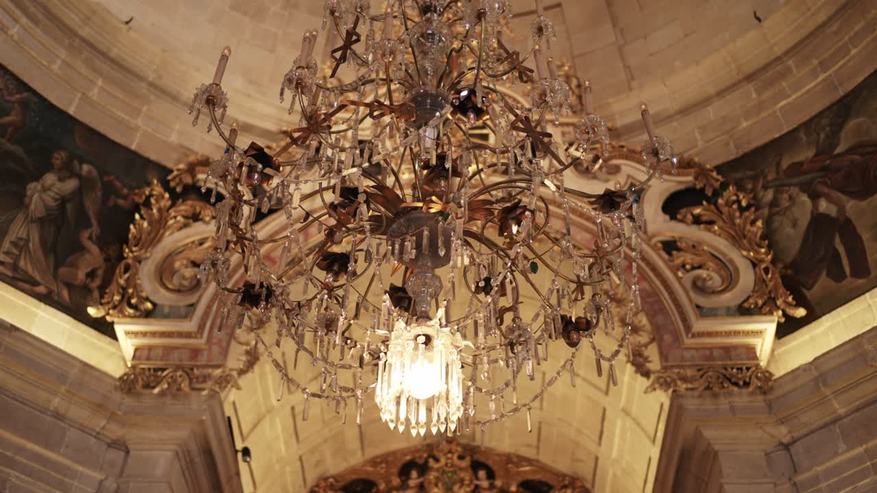 Una lámpara de araña ornamentada con detalles de cristal cuelga bajo un techo dorado de estilo barroco