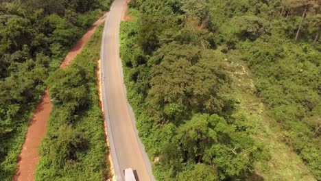 Luftdrohnenansicht-Eines-Lastwagens,-Der-An-Einem-Sonnigen-Tag-Auf-Einer-Straße-Durch-Den-Wald-Fährt,-In-Nanga-Eboko,-Haute-Sanaga,-Südkamerun