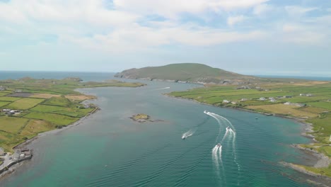 Los-Barcos-Salen-Del-Puerto-Dejando-Largos-Senderos-Blancos-Y-Curvos-En-El-Agua,-Pasando-Por-Un-Pequeño-Banco-De-Lastre-Que-Pasa-Por-La-Isla-De-Valentia-Hacia-Las-Islas-Blasket