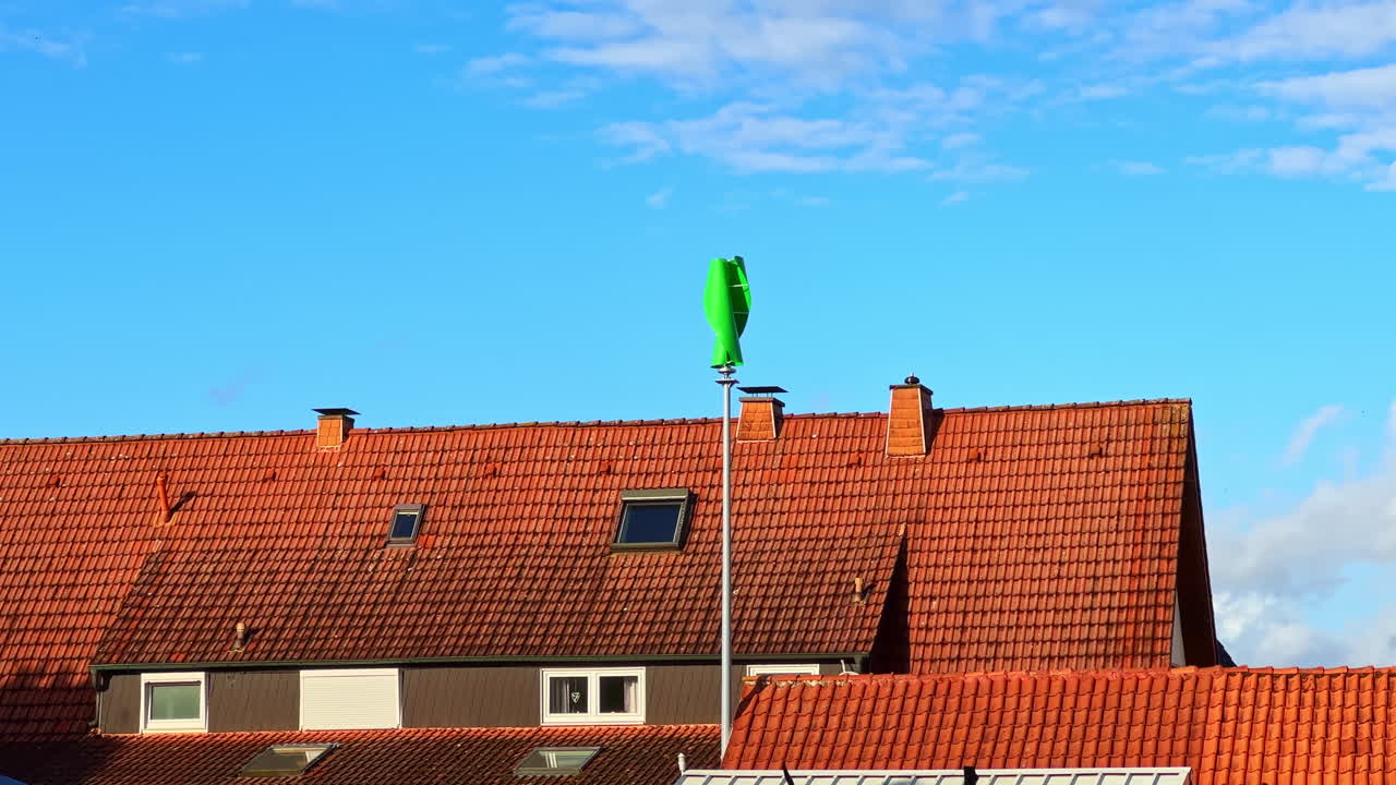 Colorful wind turbine stands tall against a blue sky and orange rooftops, symbolizing renewable energy's vibrant future