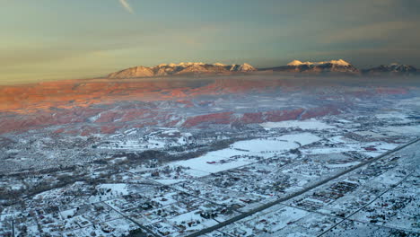 aerial winter landscape: snowy town with red rock formations and snow-capped mountains at golden hour