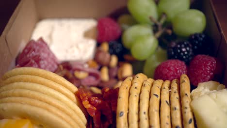 una caja de bocadillos de charcutería con carnes cocidas y curadas, galletas saladas, uvas, bayas y queso - tiro de enfoque giratorio