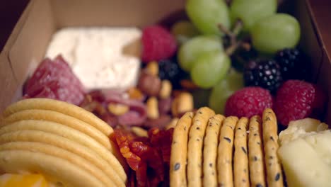 a charcutterie snack box with cooked, cured meats, crackers, grapes, berries and cheese - rotating focus pull