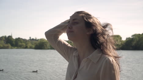 Sunset-Portrait-of-an-adorable-and-beautiful-Italian-model-walking-next-to-a-lake,-wearing-a-transparent-collar-shirt,-looking-around,-wandering-and-being-free