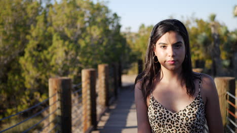 Beautiful-young-hispanic-woman-traveler-walking-in-slow-motion-along-a-wooden-path-outdoors-with-a-strong-and-serious-stare