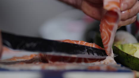 a sharp knife glides through vibrant orange atlantic salmon flesh as a chef holds the fillet steady on a white cutting board, preparing precise slices