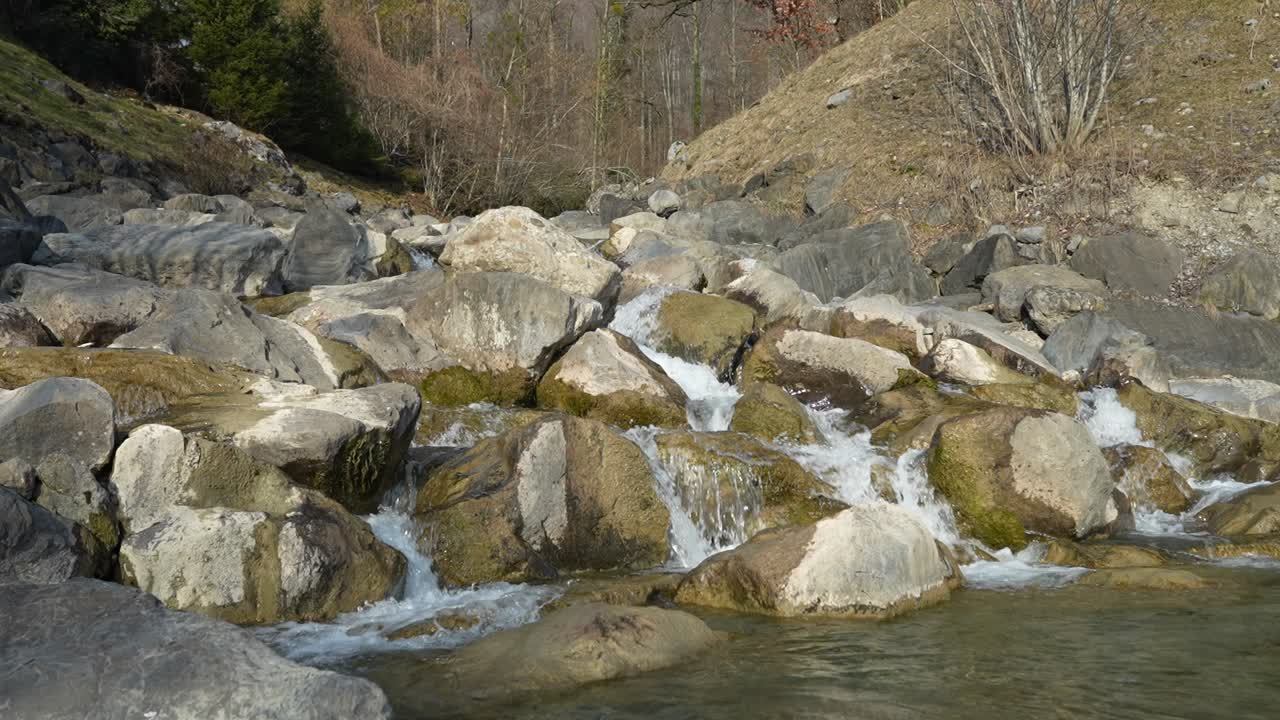 Clear water flows over mossy rocks in a rugged mountain stream, surrounded by nature and trees