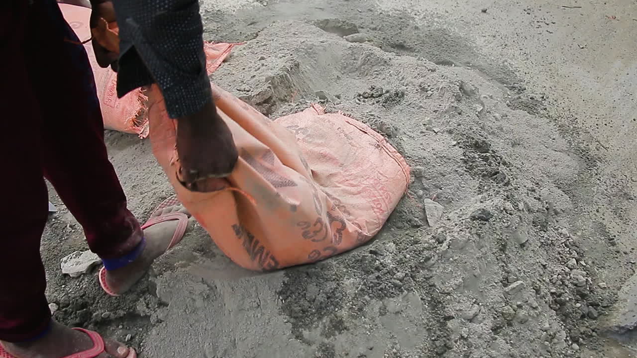 Mason worker dumping cement powder from a bag onto the ground during a construction task in Bangalore, India