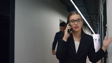 upset businesswoman speaking phone in office. frustrated manager walking hall