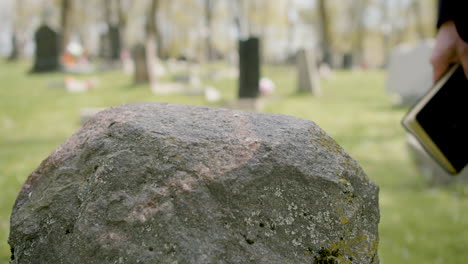 close up view of man hand touching a tombstone while holding a bible in a graveyard