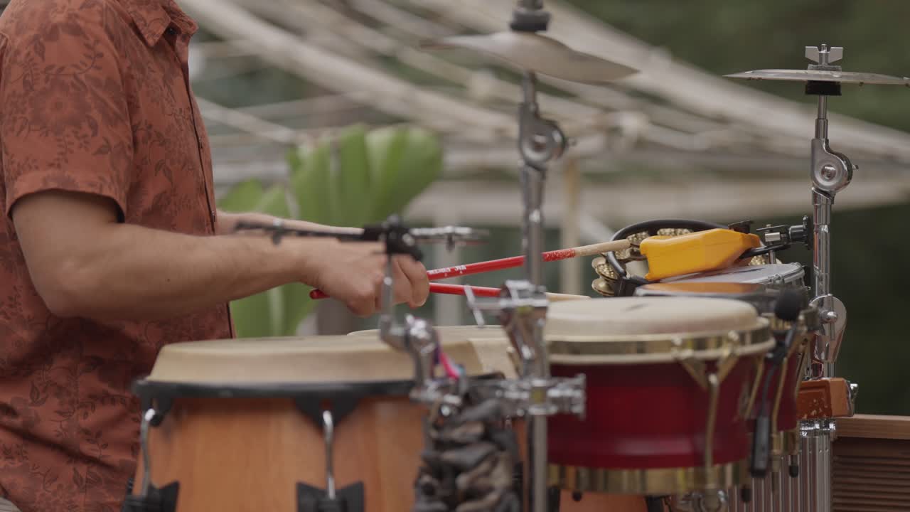 Percussionista che si esibisce con i bonghi e i piatti in un ambiente all'aperto.