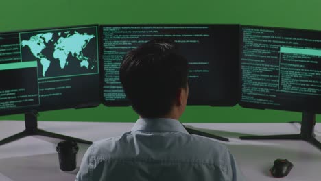 vista trasera de un desarrollador asiático cansado bostezando antes de dormir mientras escribe código con múltiples pantallas de computadora en el estudio de pantalla verde