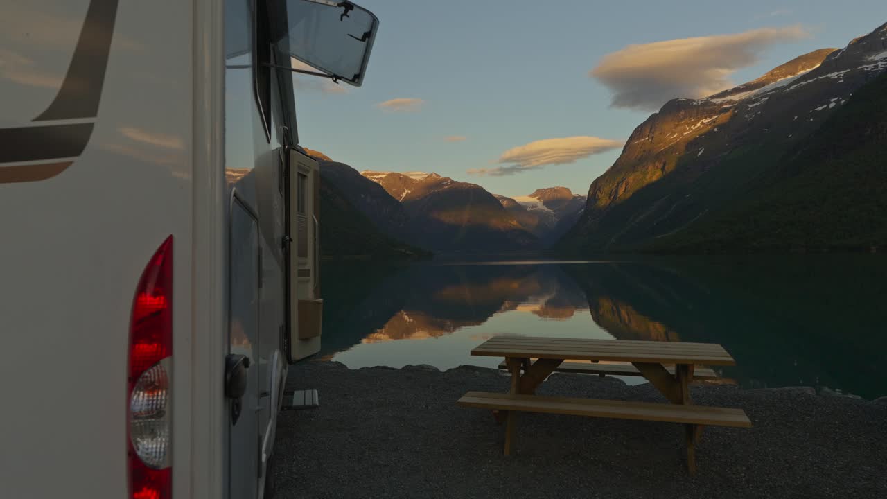 Autocaravana estacionada en la orilla de Lovatnet con un reflejo especular de las montañas del fiordo al atardecer, capturando serenos paisajes nórdicos y viajes en furgoneta camper.