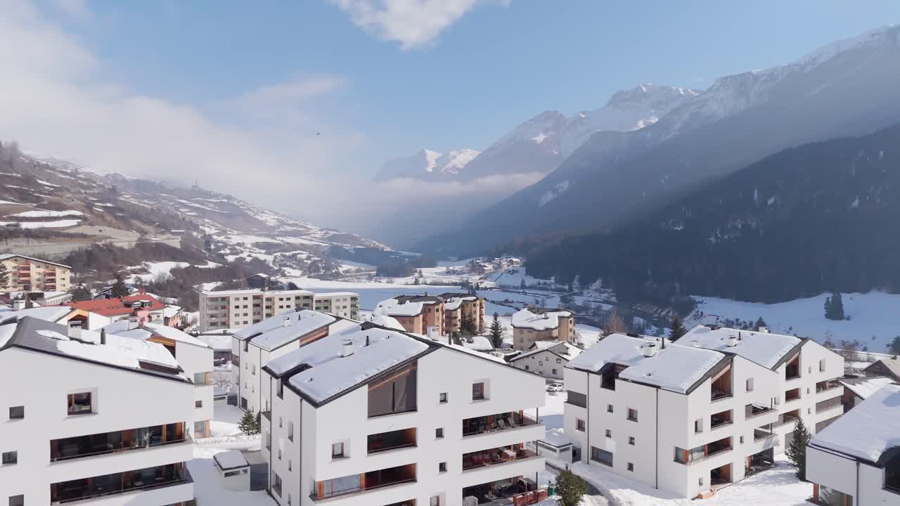 Upper class white apartment houses in swiss town. Aerial forward wide shot. Snowy mountain alps with beautiful snow-covered landscape.