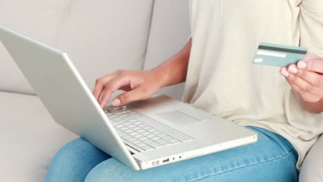 Smiling-woman-with-a-credit-card-and-a-laptop-on-a-sofa