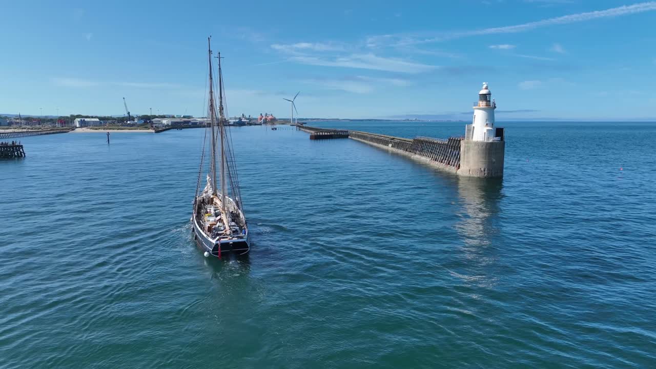 Traditional wooden tall ship entering harbour with lighthouse