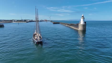 traditional wooden tall ship entering harbour with lighthouse