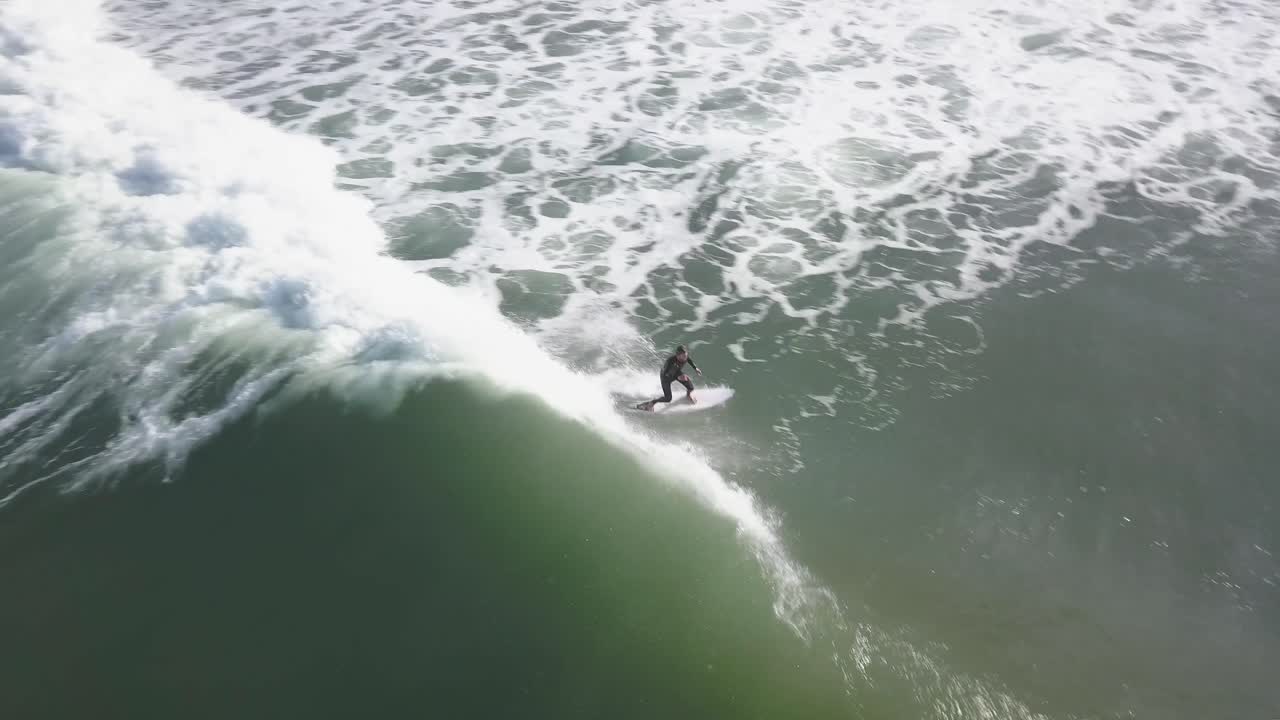 hombre en una tabla de surf como el avión no tripulado volando con ella en la ola en un día muy soleado en el surf de agua fría con una vista aérea