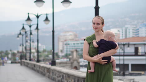 along the waterfront by the ocean on an ancient european square, a young mother walks with her baby son, watching the waves and exchanging smiles of happiness