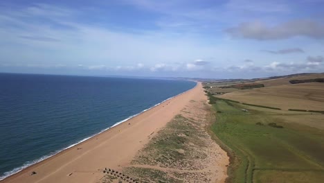 Seguimiento-Aéreo-De-Derecha-A-Izquierda-Con-Una-Ligera-Rotación-Mirando-Hacia-Arriba-La-Gran-Longitud-De-La-Playa-De-Chesil-Mirando-Hacia-El-Oeste,-Desde-La-Laguna-De-La-Flota