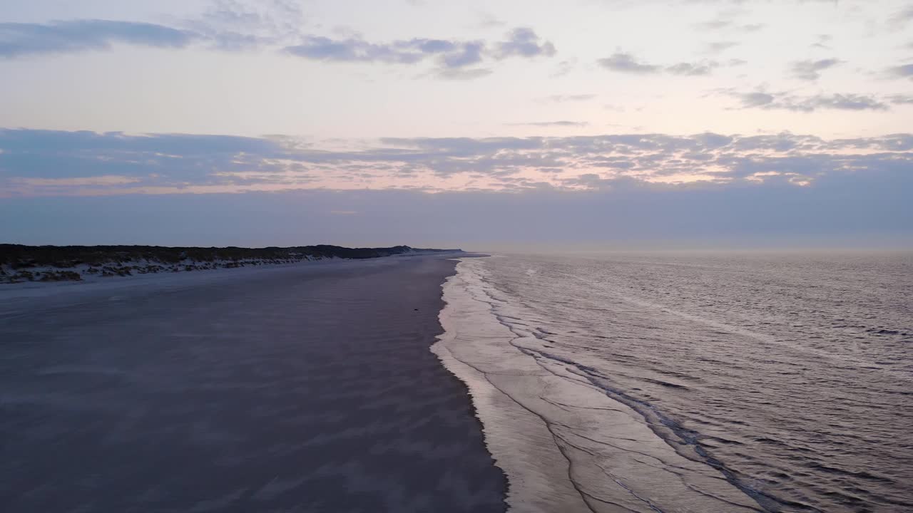 Aerial, reverse, drone shot away from a seal resting on a beach, cloudy sunset in the background, on Langeoog island, on the coast of Noordsee, in North Germany