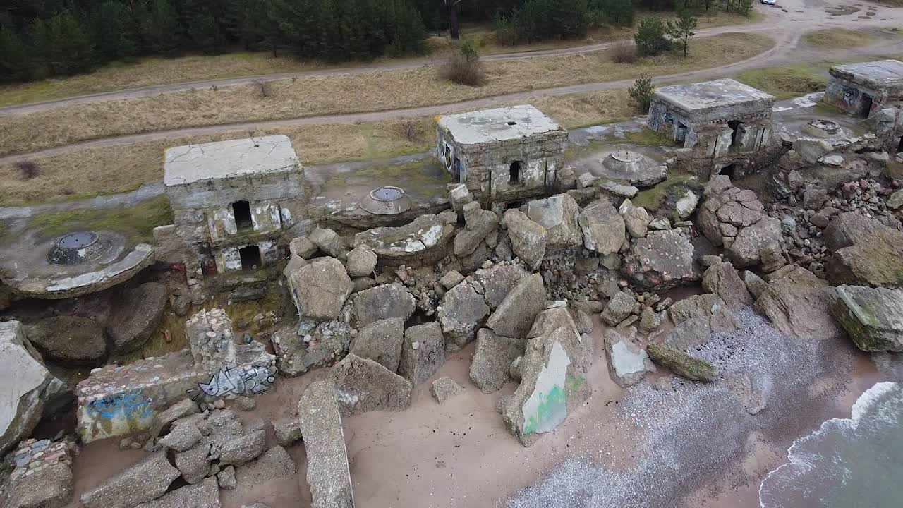 Aerial view of abandoned seaside fortification building at Karosta Northern Forts on the beach of Baltic sea in Liepaja in overcast spring day, pine wood, wide revealing drone shot moving forward