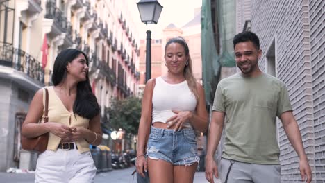 cheerful hispanic friends talking as they walk on sidewalk in city