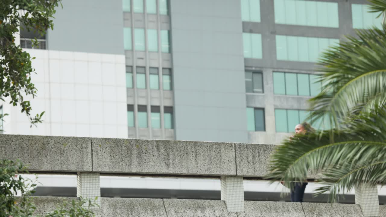 Hombre con suéter amarillo entrando por la derecha, caminando por un parapeto mientras se desplaza, mujer usando teléfono inteligente