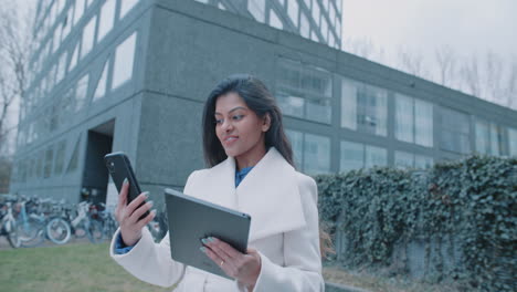 businesswoman talking on phone and using tablet near modern building
