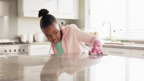 happy african american girl cleaning countertop in kitchen, in slow motion