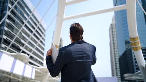 caucasian businessman holding tablet using a smartphone walking in the city