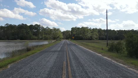 Punto-De-Vista-De-Conducción-Lenta-En-Medio-De-Una-Carretera-Pavimentada-Con-Líneas-Amarillas-Y-Pasando-Un-Suspiro-Amarillo-De-Giro-A-La-Izquierda