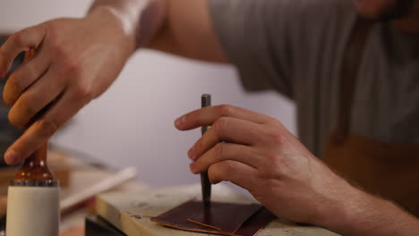 worker taps punch tool with hammer to make holes in leather