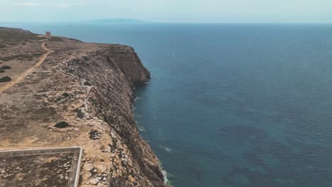 Flying-above-arid-rocky-clifftop-towards-La-Torre-Des-Garroveret-ancient-watch-tower