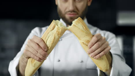 chef breaking french bread in slow motion. closeup baker hands breaking bread.