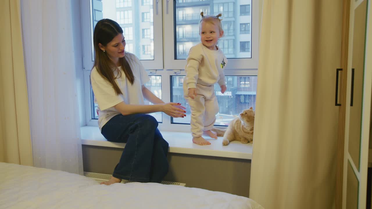 Young Mother and Toddler Playing with Cat on Windowsill