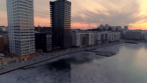 aerial view of modern office buildings next to frozen bay in stockholm, sweden. drone shot flying up in front contemporary residential district at sunset